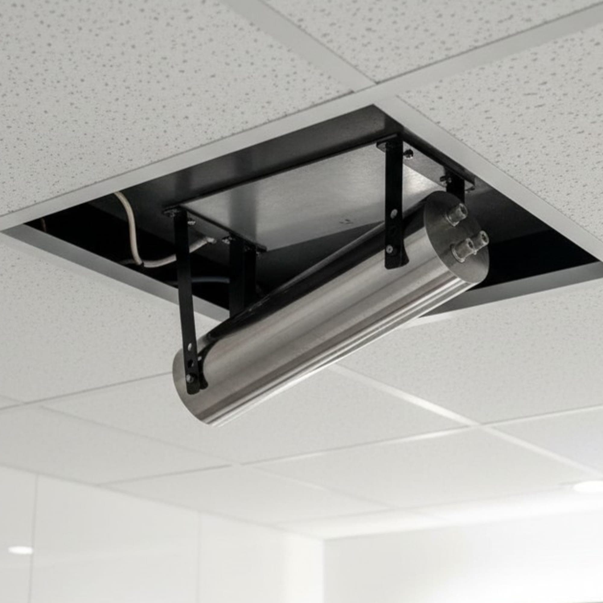 Stainless cylinder mounted in the suspended-ceiling void of a finished bathroom, accessed via a removable panel